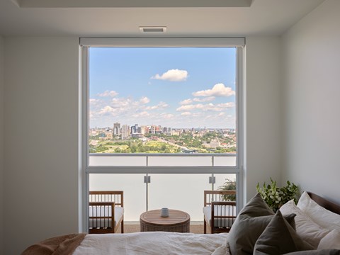 A bedroom with a large window overlooking a cityscape.