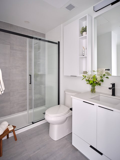 A modern bathroom with a toilet, sink, and a glass shower door.