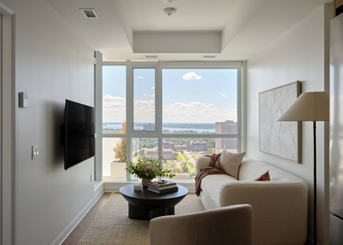 A living room with a flat screen TV mounted on the wall and a large window with a view of the city.