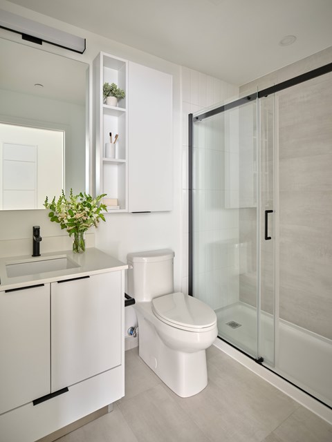A white toilet sits in a modern bathroom next to a sink and a glass shower door.