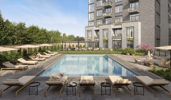 A large pool surrounded by lounge chairs and umbrellas in front of a building.