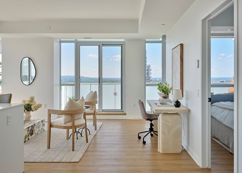A room with a desk, chairs, and a view of the city through the windows.
