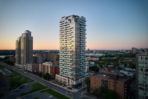 A tall, modern glass building stands in the foreground of a cityscape at dusk.