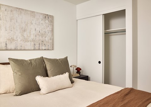 A bed with a brown pillow and a white pillow is in front of a painting.