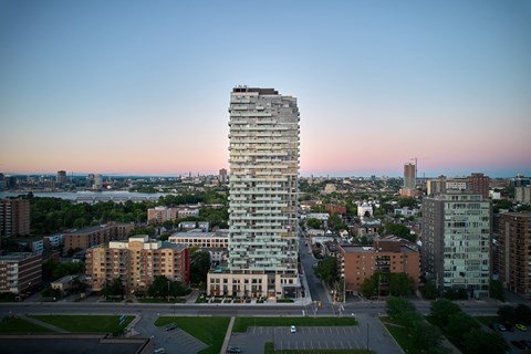 A tall, modern building stands in the middle of a cityscape at dusk.