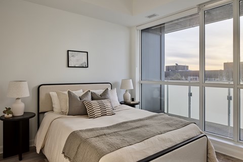 A bedroom with a large bed, a nightstand with a lamp, and a picture on the wall.