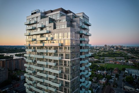 A tall, modern building with many windows and balconies is shown from a distance.