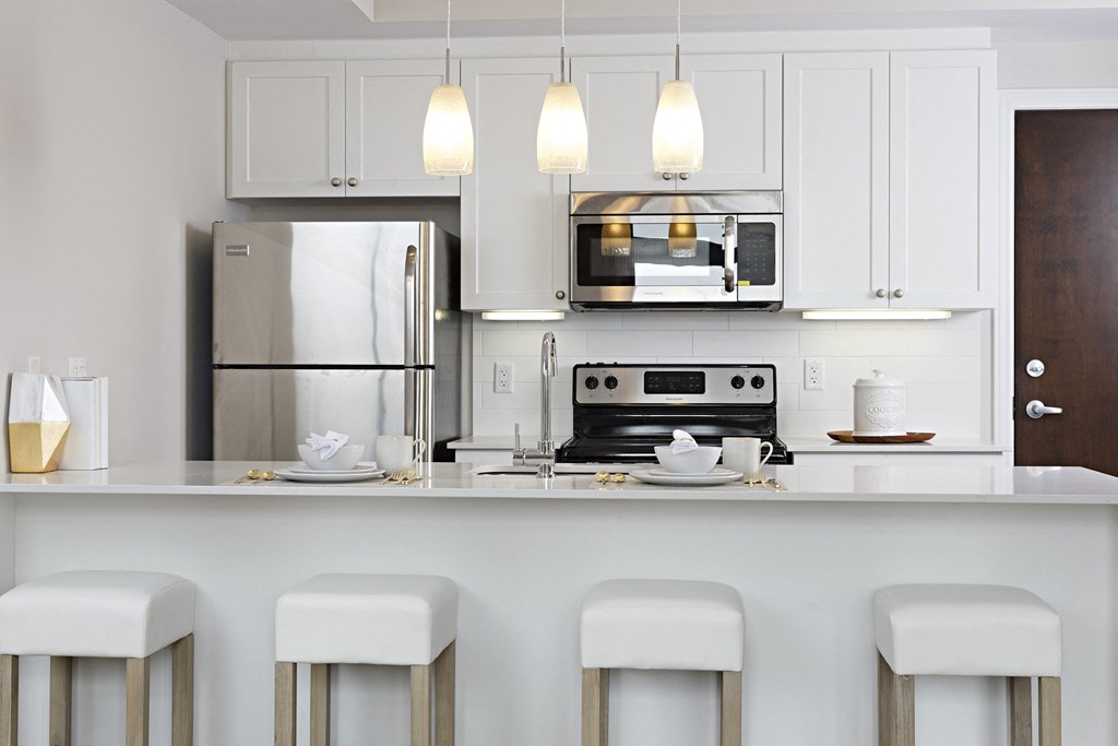 a kitchen with white cabinets and a bar with white stools