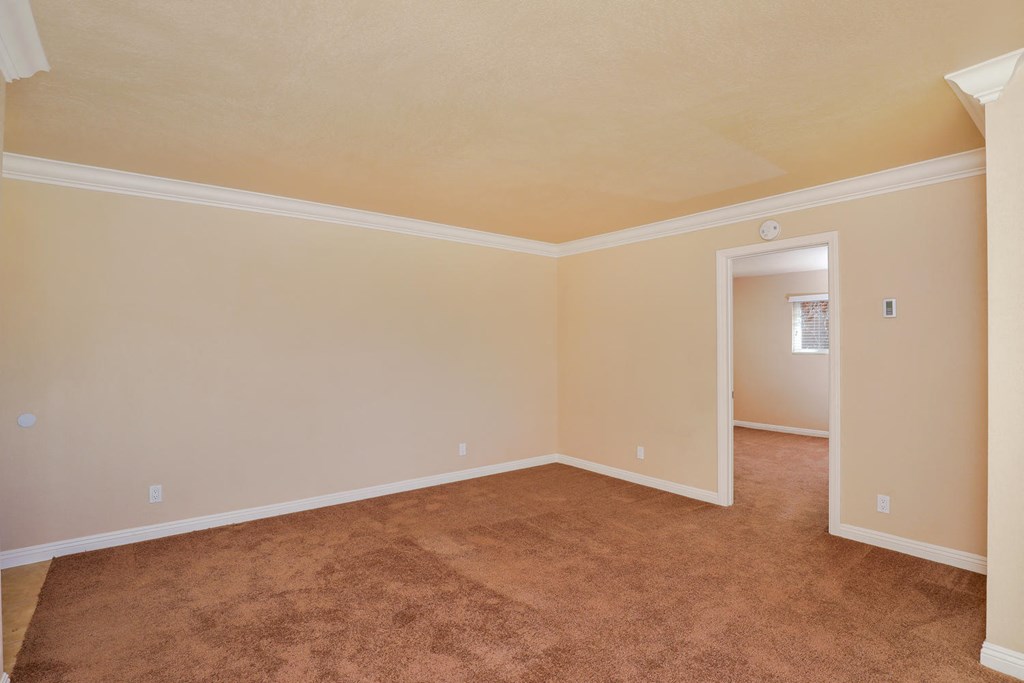 an empty living room with carpet and a door to a bedroom