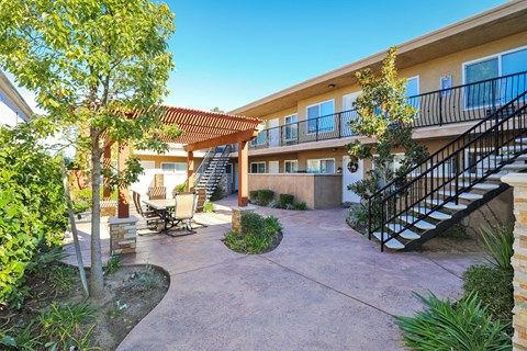 a patio with a staircase and trees in front of a building
