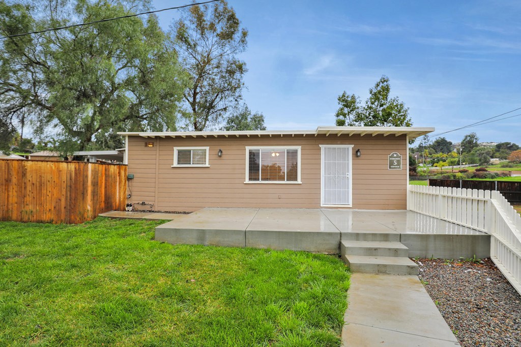 a small tan house with a yard and a white fence