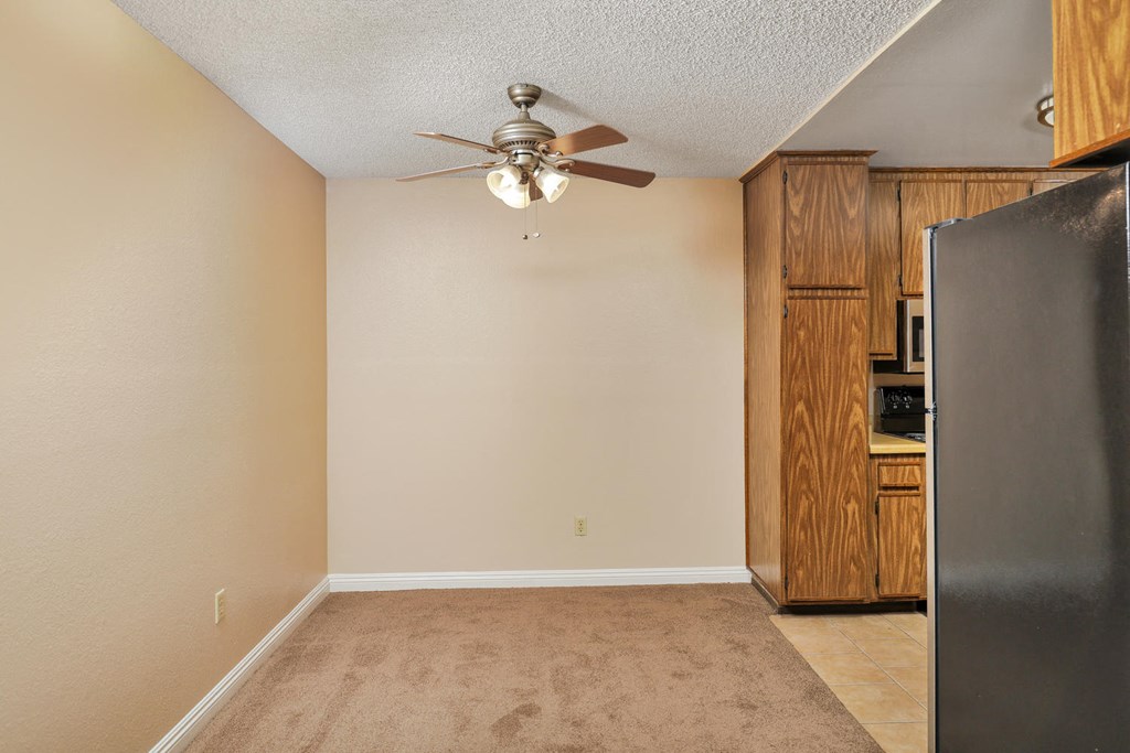 an empty living room with a ceiling fan and a refrigerator