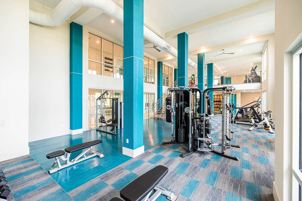 a gym with cardio equipment and weights in a building with windows