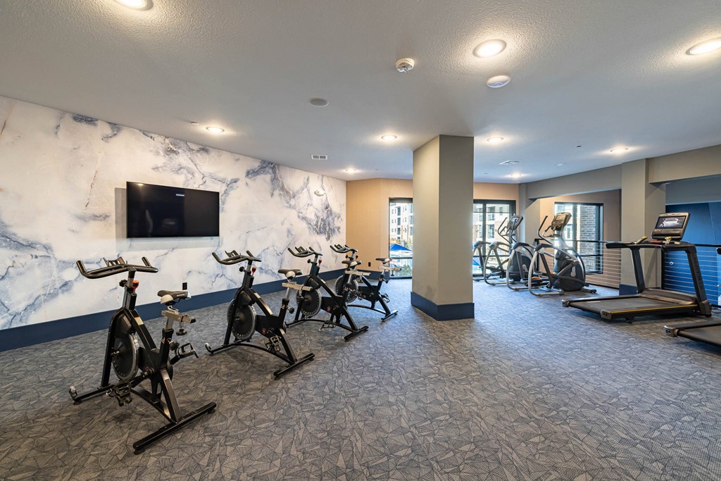a gym with exercise equipment and a marble wall with a tv
