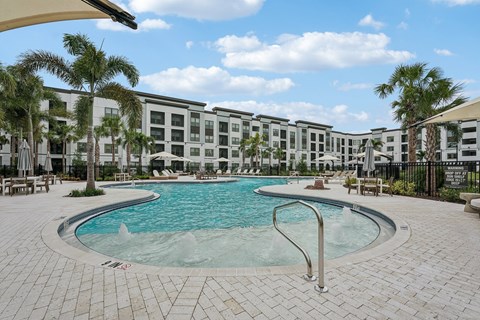 A pool surrounded by palm trees and a building in the background.