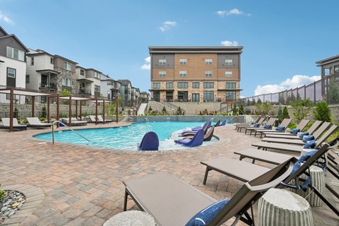 A swimming pool surrounded by lounge chairs and umbrellas in a residential area.