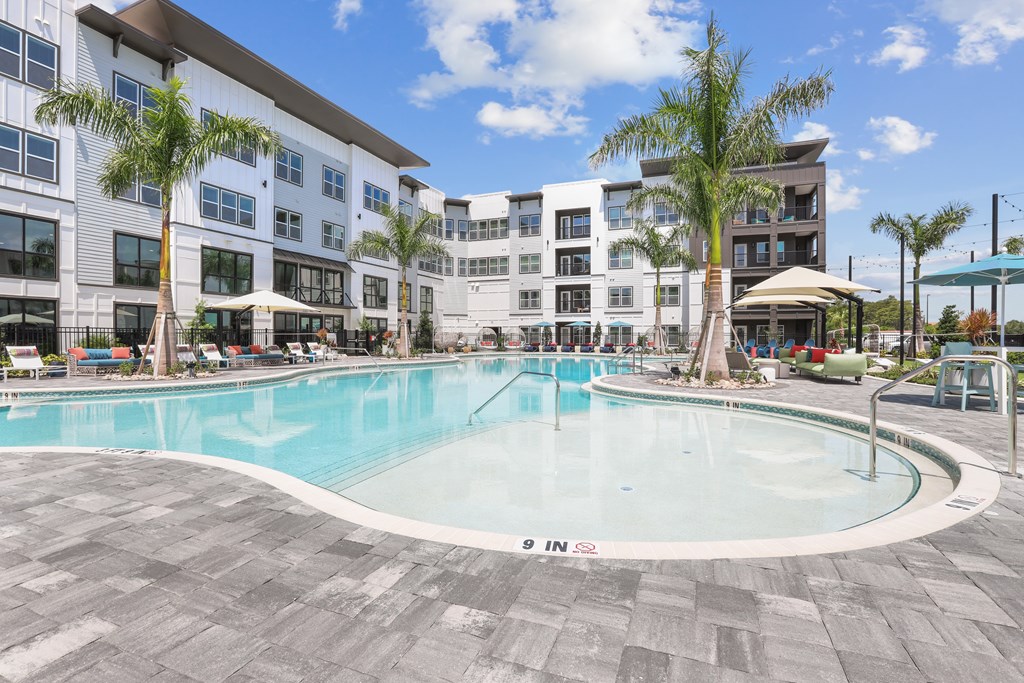 A large swimming pool surrounded by a tiled floor and a building in the background.