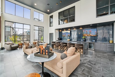 A modern living room with a large window and a kitchen area in the background.