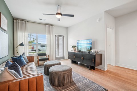 A living room with a brown leather couch, a round ottoman, and a flat screen TV mounted on the wall.