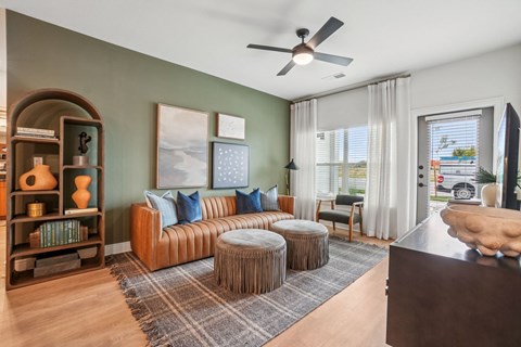 A living room with a brown couch, a round table, and a fan on the ceiling.