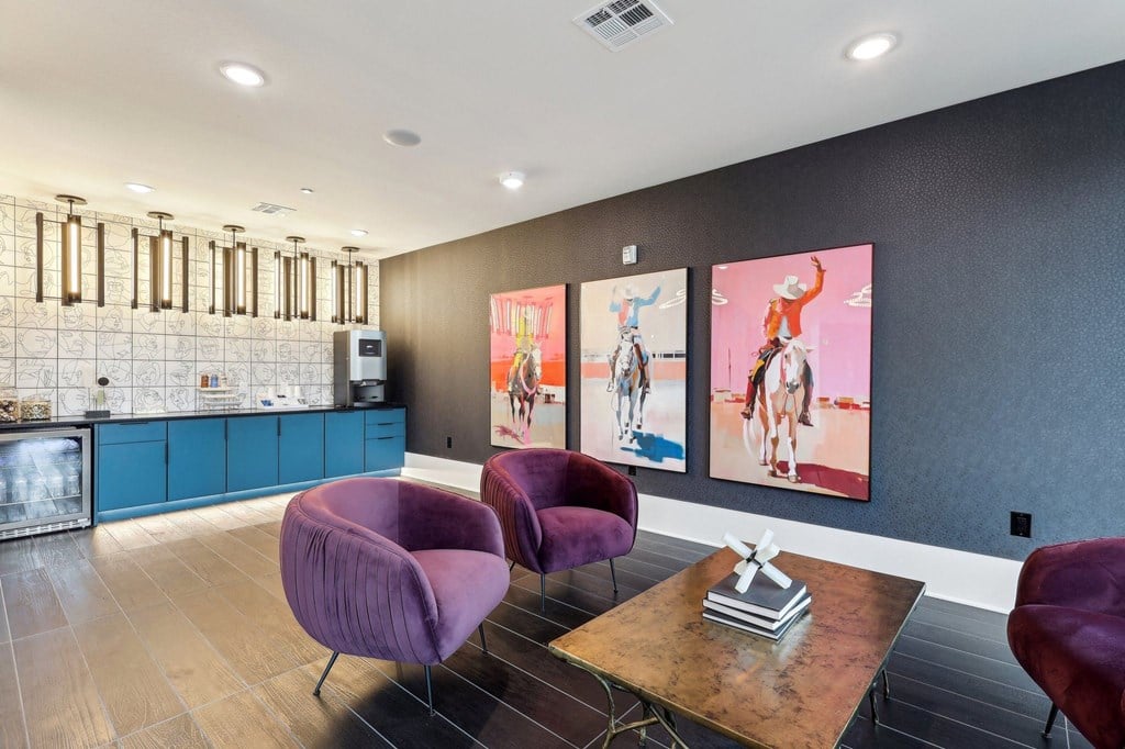 a lounge area with purple chairs and a table and paintings on the wall