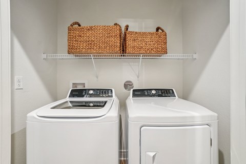 Two white washing machines are on a shelf in a laundry room.