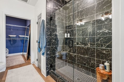 A bathroom with a marble tile shower and a blue shower curtain.