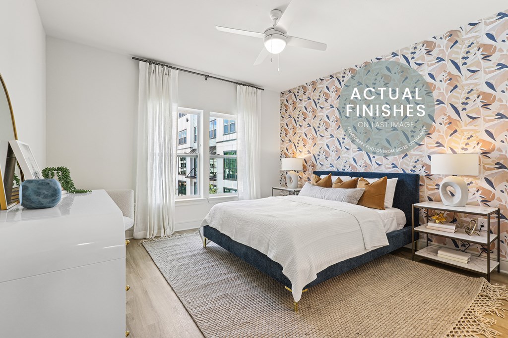 A bedroom with a bed, a dresser, and a wallpapered wall with a pattern of leaves.