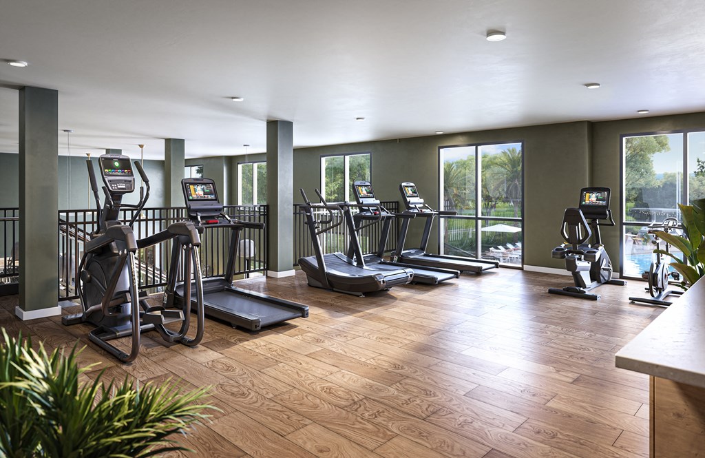 a gym with cardio equipment on a wooden floor and large windows