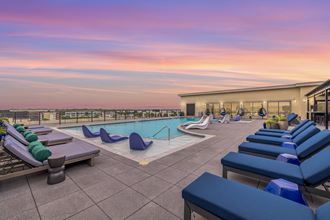 a rooftop pool with blue lounge chairs and a sunset in the background
