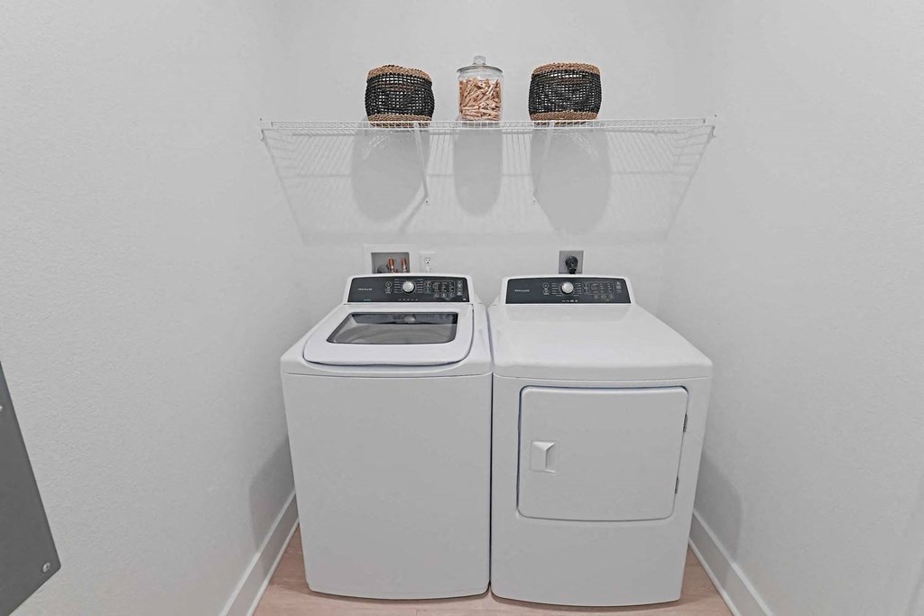 two washes and a dryer in a laundry room with a shelf above them