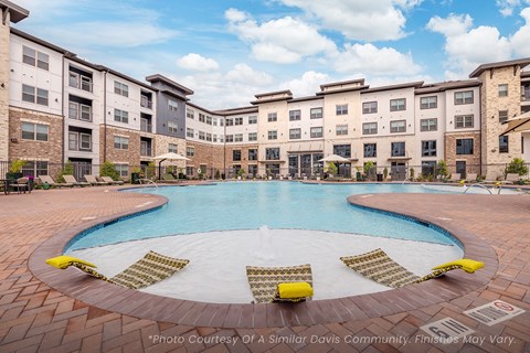 A large swimming pool surrounded by lounge chairs in front of apartment buildings.