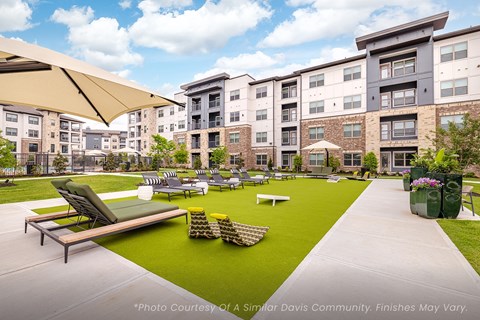A sunny day at a community with apartment buildings, a green lawn, and a shaded seating area.