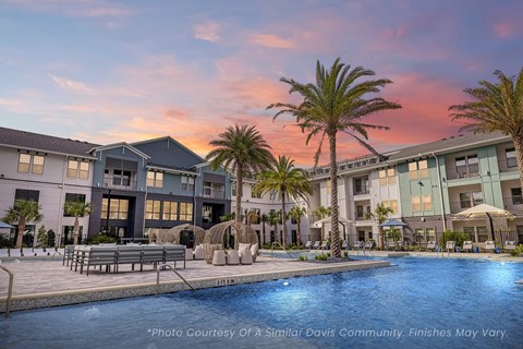 A beautiful view of a swimming pool surrounded by palm trees and lounge chairs at a residential complex.
