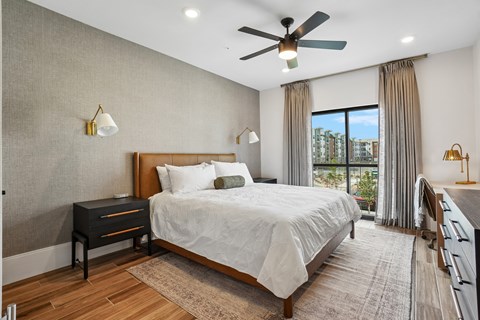 A bedroom with a large bed, a ceiling fan, and a view of the city.