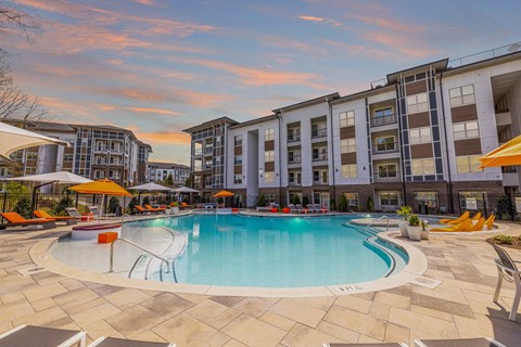 a swimming pool with chairs and umbrellas in front of an apartment building