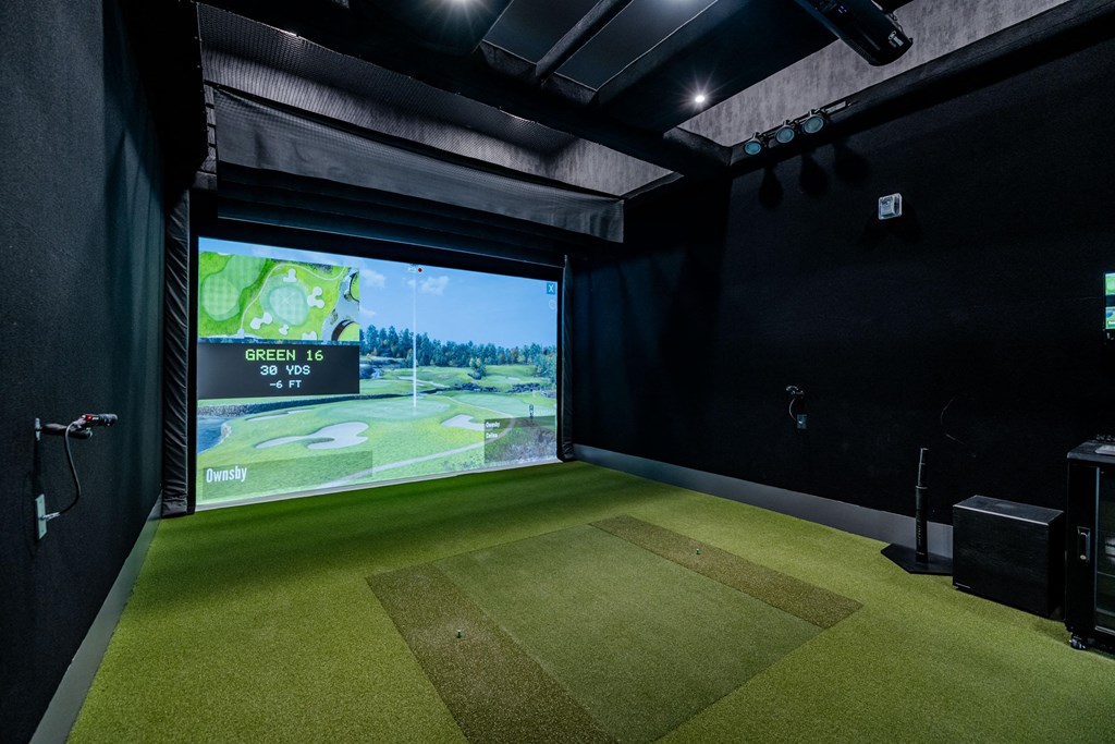 a golf simulator in a black room with a view of the course on the screen