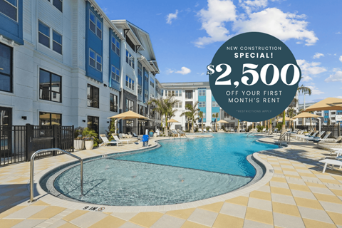 A swimming pool surrounded by a tiled floor and a building in the background with a sign offering $2,500 off the first month's rent.