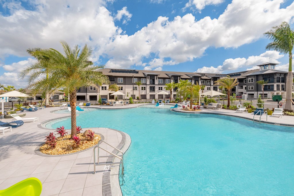 a large swimming pool with palm trees and buildings in the background