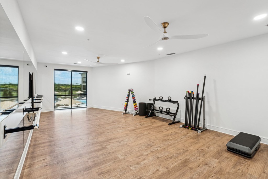 A spacious room with a wooden floor, a ceiling fan, and exercise equipment.