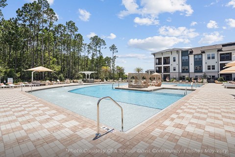 A large outdoor swimming pool surrounded by a tiled patio and trees.