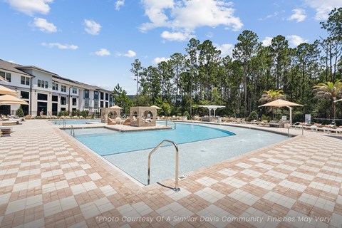 A large pool surrounded by a tiled patio and umbrellas.