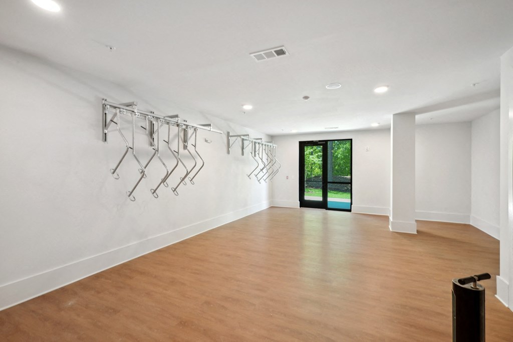 a living room with a wood floor and a white wall with a rack of clothes