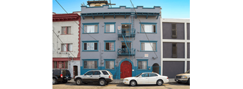 A blue building with a red door and a balcony with a railing.