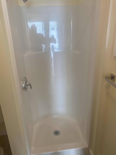A white shower stall with a drain in the bottom.