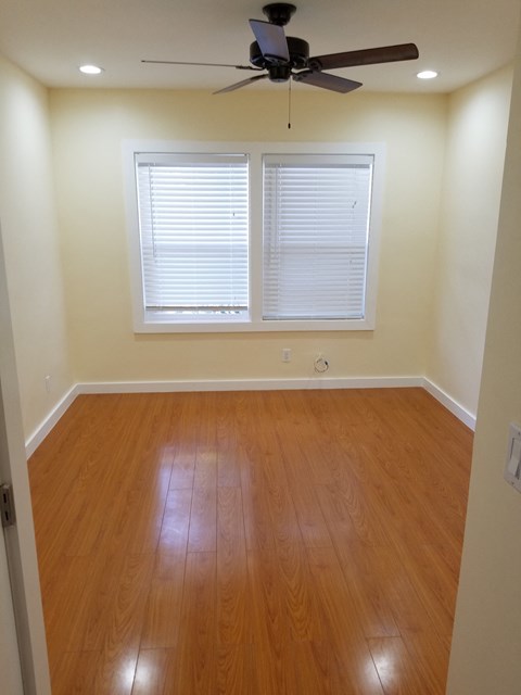 A room with a ceiling fan and a window with blinds.
