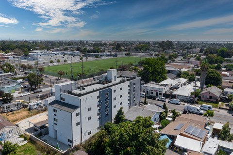 A large white building with a flat roof is surrounded by trees and other buildings.