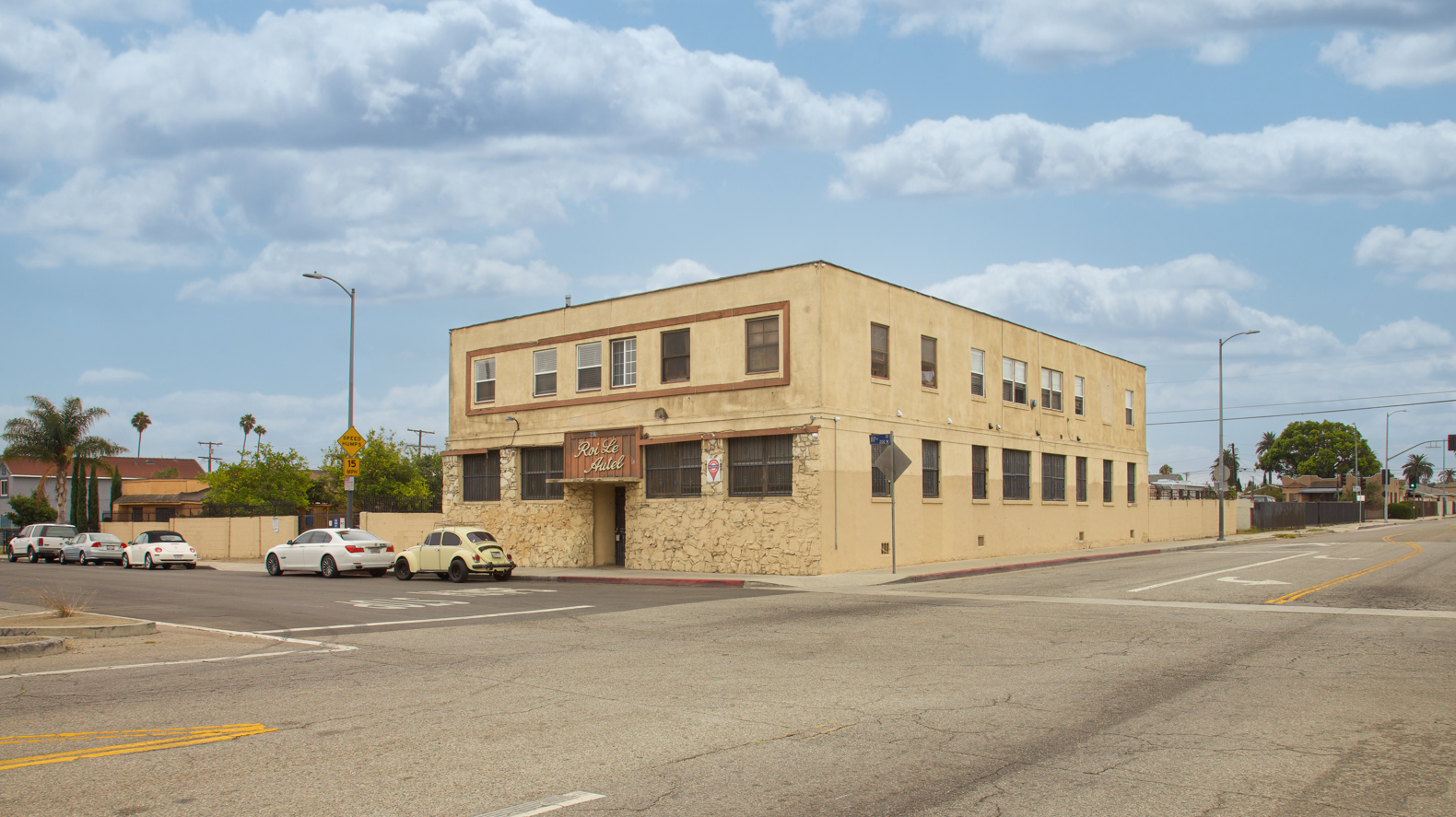 A building with a yellow facade is situated on a street corner with cars parked in front.