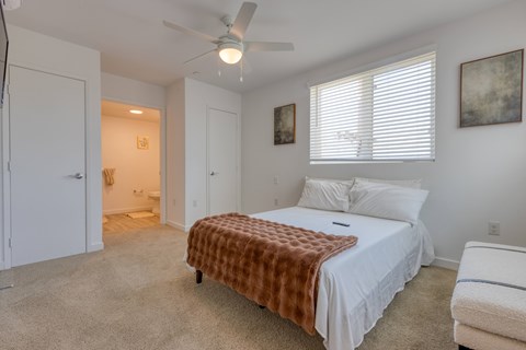 A bedroom with a bed covered in a brown blanket and a ceiling fan.