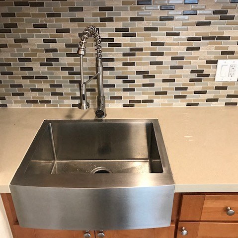 A stainless steel sink with a faucet and a tile backsplash.